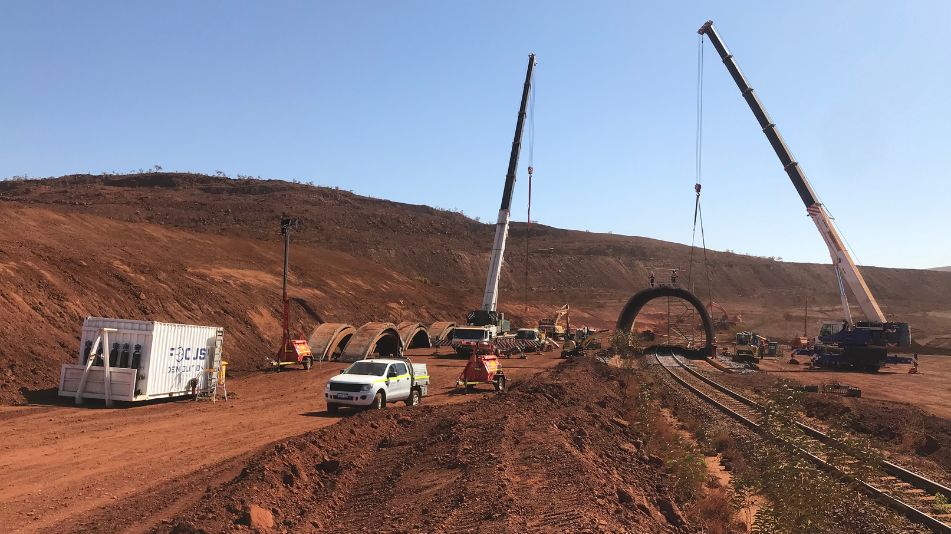 Wide shot of the demolition of rail tunnel bridge in an operating live mine site featuring heavy machinery.